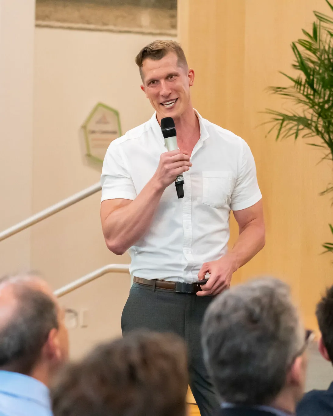 Jesse Henry speaking into a microphone at Greentown Labs, in a white shirt, with an audience in the foreground.